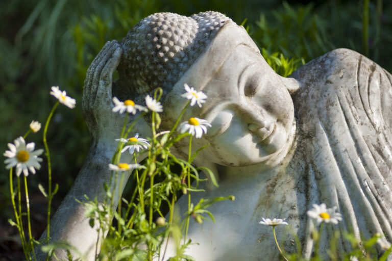 Nepal Himalaya Park, bestehend aus buddhistischer Stupa und hinduistischem Pavillon. Nahaufnahme liegender Buddha in weiß in einem Blumenbett.