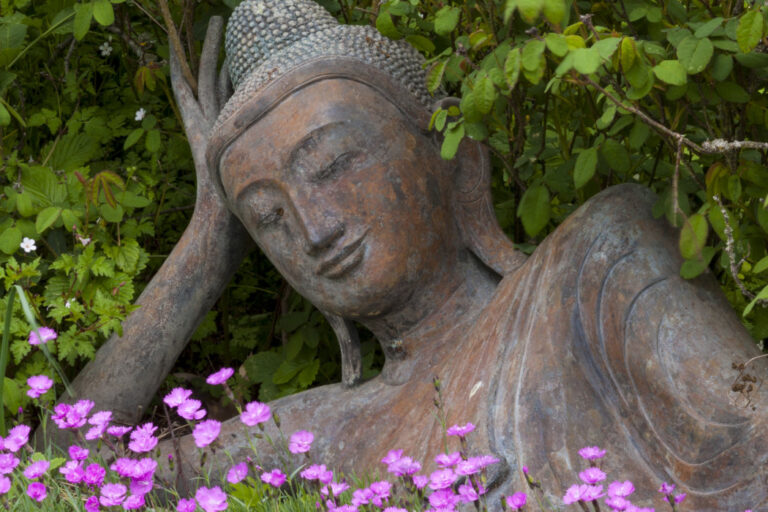 Nepal Himalaya Park, bestehend aus buddhistischer Stupa und hinduistischem Pavillon. Nahaufnahme liegender Buddha aus Bronze in einem Blumenbett.