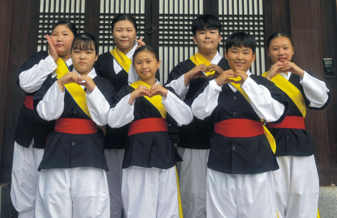 Kinder der koreanischen Kunstgruppe Hansori Gruppe von Kindern in traditioneller Kleidung, die vor einem Gebäude mit ihren Händen Herzzeichen formen